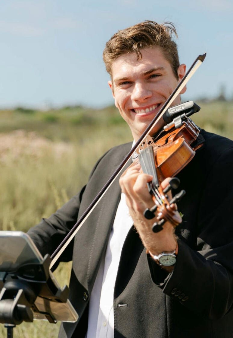 Violinist in a black dress holding a violin, lit by warm light.